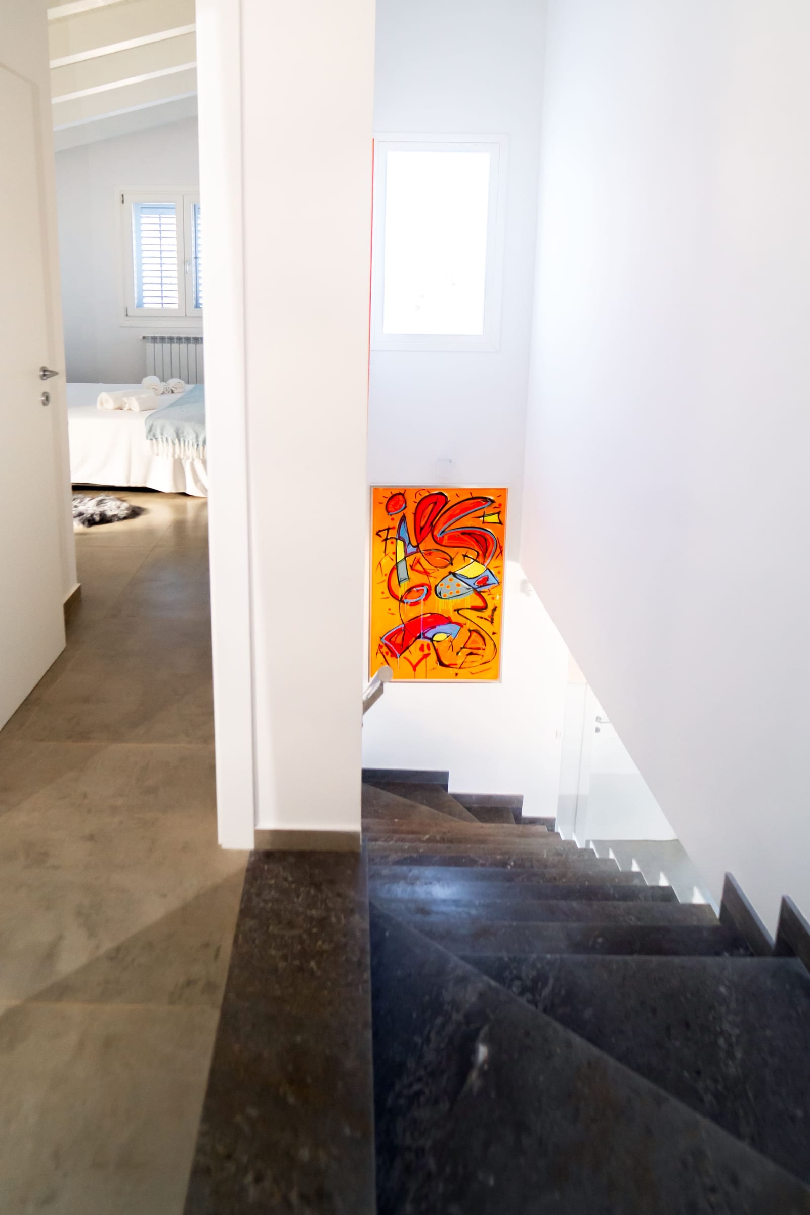 Landing with dark stairs and an orange abstract painting; an open door leads into a bedroom