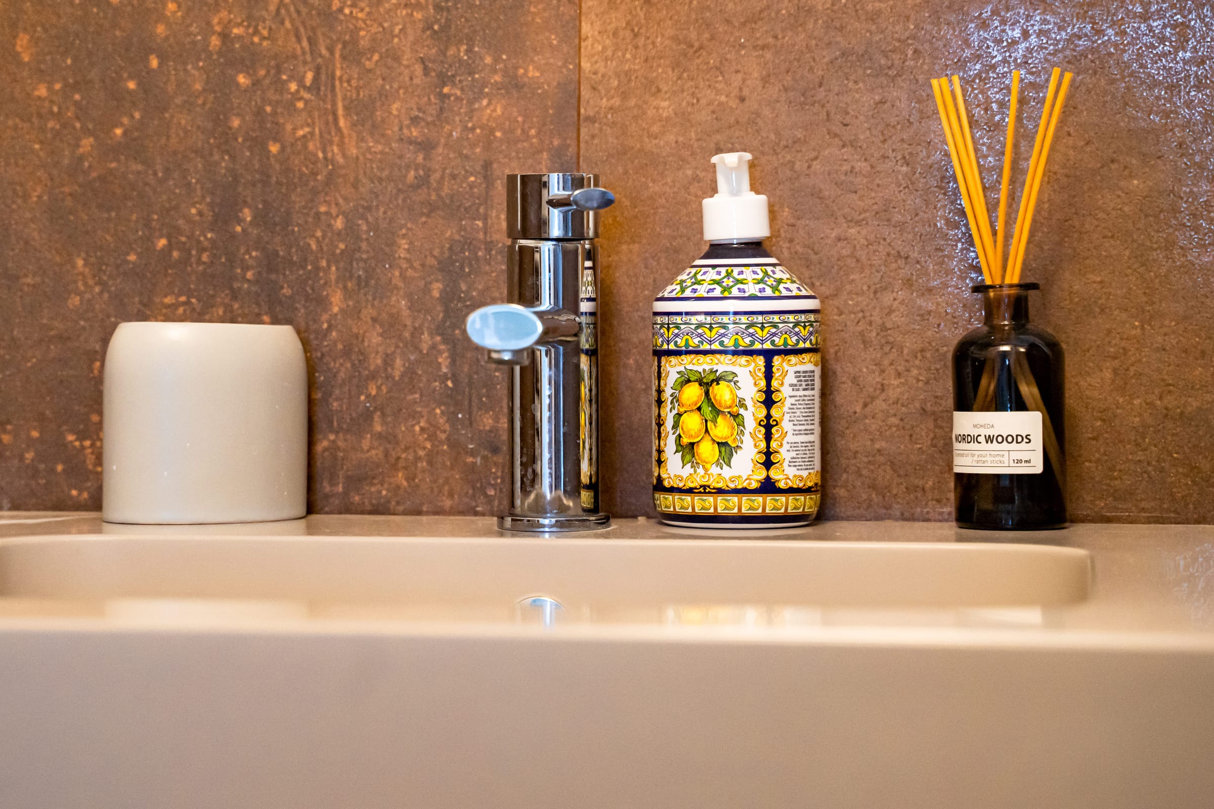Soap dispenser painted with lemons beside a chrome tap, set against rust-brown tiles